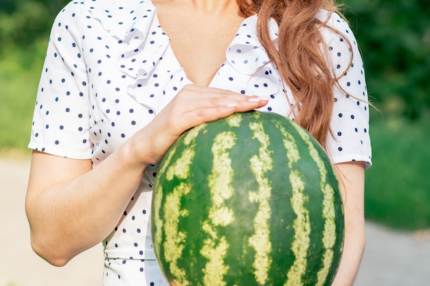 Foto hele watermeloen close-up in handen van jonge vrouw op groene natuur achtergrond.