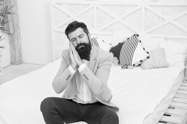 Helemaal aangekleed en nergens heen Slaperige hipster zit op bed Bebaarde met slaperige blik in formalwear Daydream Zich moe en slaperig voelen Wachten maakt hem slaperig