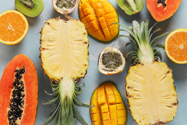 Helften van tropisch fruit papaja, mango, ananas, kiwi, sinaasappel en passievrucht op een lichtblauwe achtergrond, bovenaanzicht