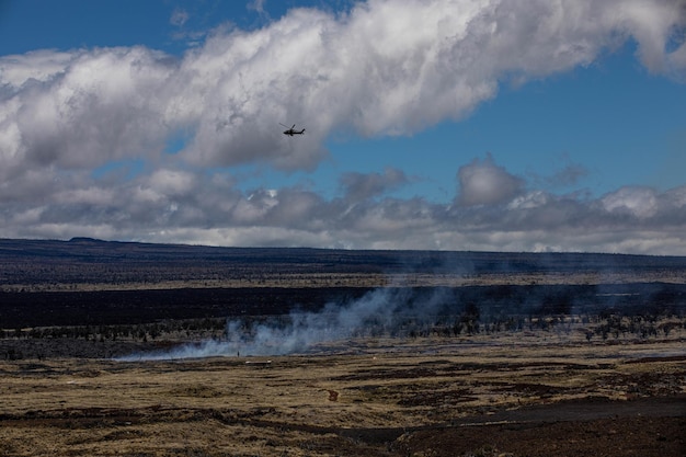 A helicopter flies over a dry grass field.