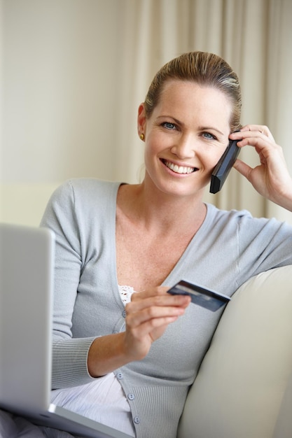 Foto l'inferno non indovina mai cosa gli sto procurando una giovane donna che parla al cellulare mentre tiene in mano una carta di credito e si siede con un laptop