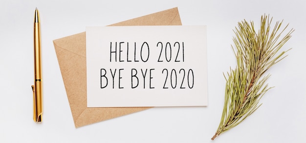 Hello 2021 bye bye 2020 note with envelope, spruce branch and gold pen on white surface. merry christmas and New Year concept