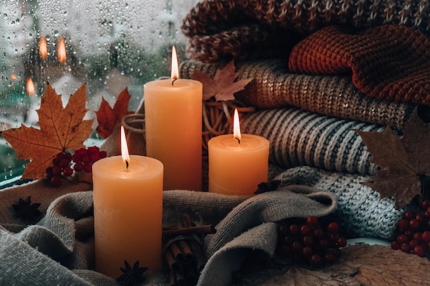 Hello Fall celebrating autumn holidays at cozy home on the windowsill Hygge atmosphere Thanksgiving leaves spices and candle on cozy knitted sweater in warm yellow lights Raining Outside the window