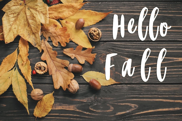 Hello Fall Text Знак Hello Autumn на ярких красочных осенних листьях с желудями и орехами на деревенском деревянном столе. Плоская планировка Осеннее изображение Макет поздравительной открытки Атмосферное изображение