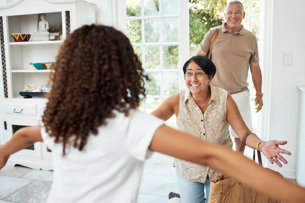 Hello home and girl running to grandparents by door excited for bonding spending time and relationship Family happy and grandmother grandfather and child embrace for greeting welcome and visit