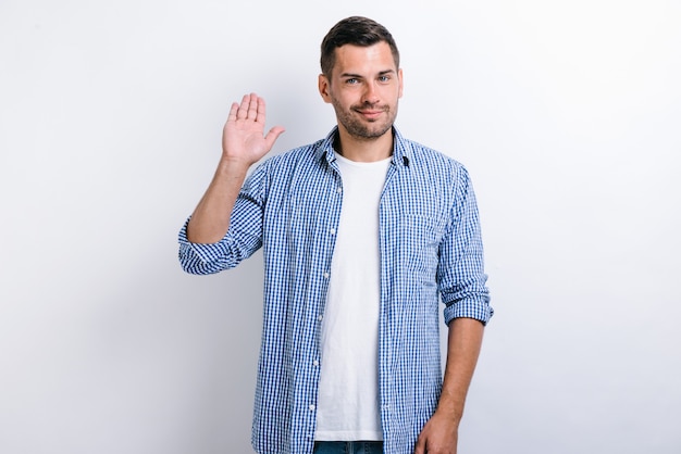 Hello! portrait of good-natured positive bearded man waving hand and friendly smiling at camera, making hi welcome gesture. indoor studio shot isolated on white background