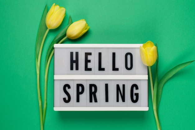 Hello Spring - текст на лайтбоксе с желтыми тюльпанами на зеленом фоне.