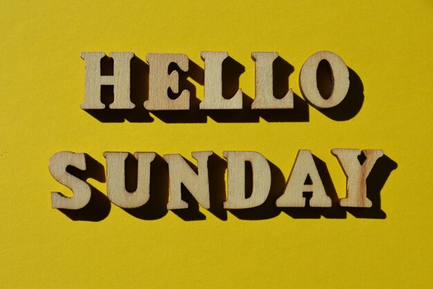 黄色い背景に隔離された木製のアルファベットの文字で"Hello Sunday"の言葉