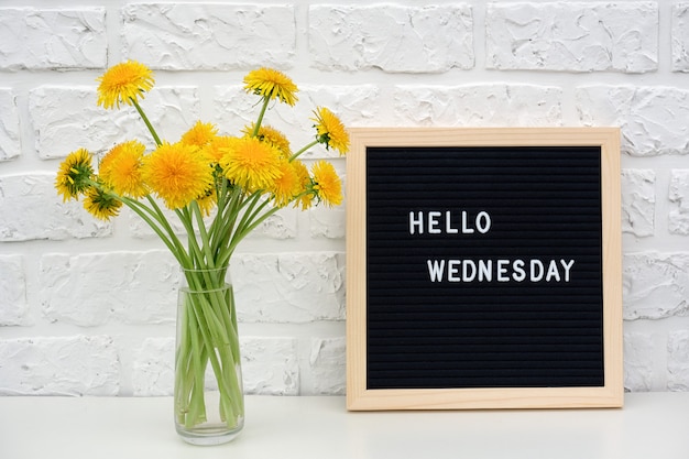 Hello Wednesday words on black letter board and bouquet of yellow dandelions flowers 