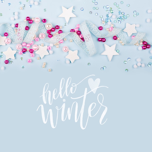 Hello Winter with cute decoration:  lace ribbon, stars, sequins and pink pearl beads  on blue background. Flat lay, top view.