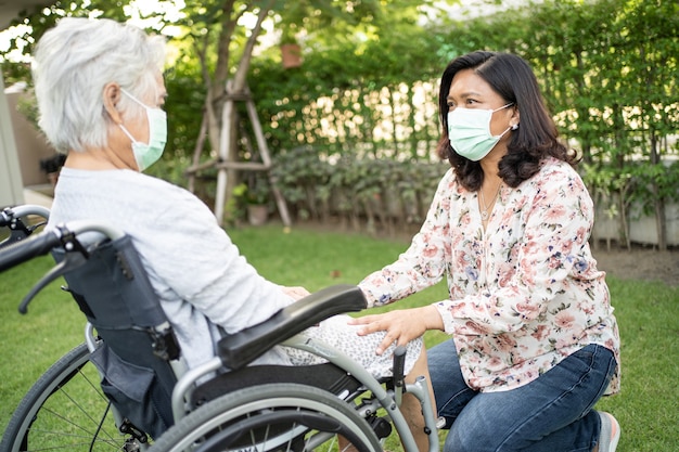 공원에서 covid19 코로나바이러스를 보호하기 위해 휠체어를 탄 아시아 노인 여성을 도와주세요