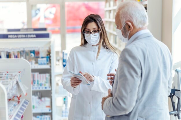 薬剤師の助けを借りて。眼鏡をかけた女性薬剤師が薬箱と使用説明書を持っています。彼女は何か他のことを説明している男を見ます。どちらも保護マスクを着用しています