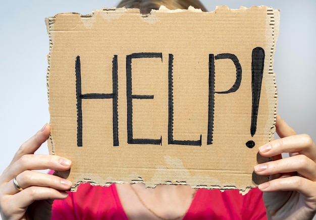 HELP the girl is holding a piece of cardboard with the inscription help