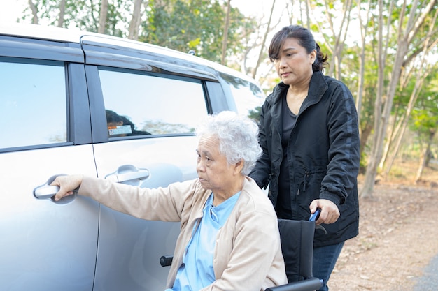 車椅子に座っているアジアの年配の女性患者が彼女の車に行く準備を手伝ってください