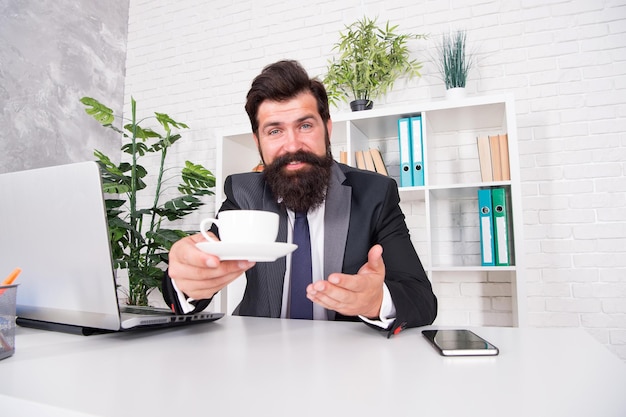 Help yourself please Happy businessman serve hot cup at desk Project manager drink tea during work break Break time Enjoying break during work day Productivity soars after coffee break