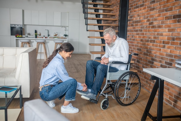 Helpende echtgenoot. Donkerharige jonge vrouw helpt haar gehandicapte man zijn snickers te strikken