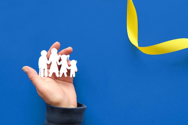 Helpende hand met Oekraïens familiepapier silhouet Plat lag bovenaanzicht Copyspace tekst plaats op blauwe achtergrond met geel lint