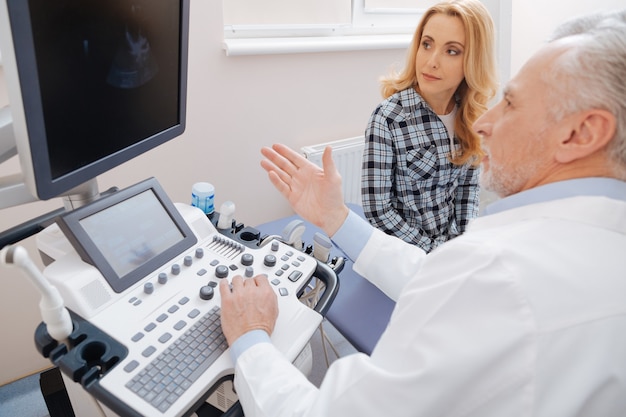 Helpful qualified senior sonographer working in the clinic and consulting the patient while providing ultrasonic scanning