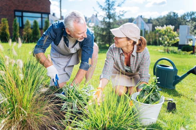 Helping in garden. Mature handsome man wearing white gloves helping his beautiful young wife in the garden