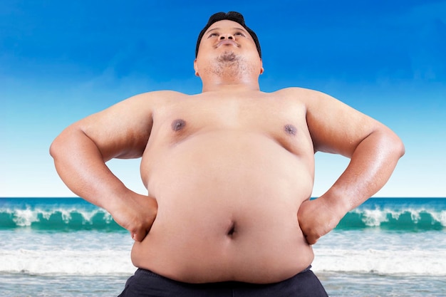 Hemdloze man die met zijn handen op de heup staat op het strand tegen de lucht