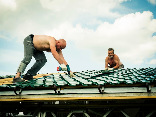 Hemdloze mannen werken op het dak tegen de lucht.