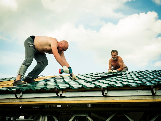 Foto hemdloze mannen werken op het dak tegen de lucht.