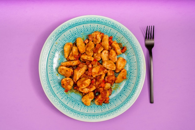 Hemelse plaat van Gnocchi met rode saus op een paarse tafel. Begeleidt een moderne zwarte vork. Typisch Italiaans eten