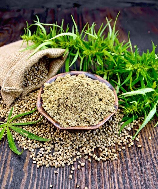 Hemp flour in a bowl and the grain in the bag on the table green cannabis leaves on the background of dark wood planks