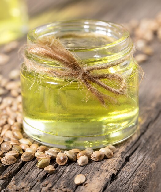 Hemp oil in glass jar and grains of cannabis on background of old wooden boards close-up.