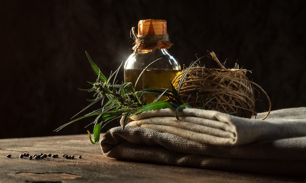 Hemp product concept. Bottle of oil, textiles, rope and cannabis plant on a wooden table.