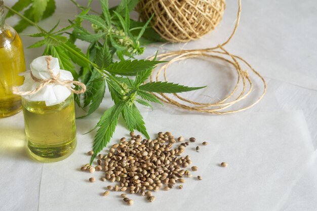 Hemp products concept. Bottles with cannabis oil, a skein of thread and a green plant on a white background