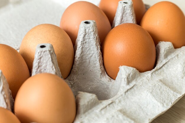 Hen eggs in open cardboard egg carton on kitchen table light copy space background. Healthy organic food and diet concept.