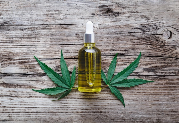 Hennep cbd olie serum in glazen druppelflesje met cannabis bladeren. Cannabisblad met huidverzorging cosmetisch product CBD-olie op oude houten ondergrond.