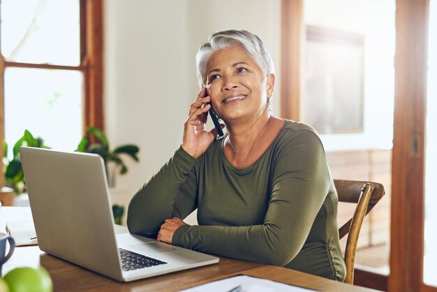 Her broker just called with some more good news Shot of a mature woman talking on a cellphone while working on a laptop at home