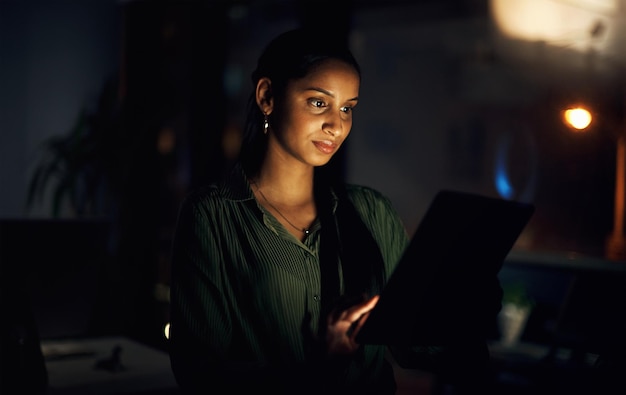 Photo her connections are always awake with her shot of a young businesswoman using a digital tablet in an office at night