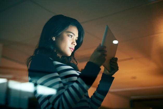 Her determination runs high even through the dark Shot of a young businesswoman working late on a digital tablet in an office