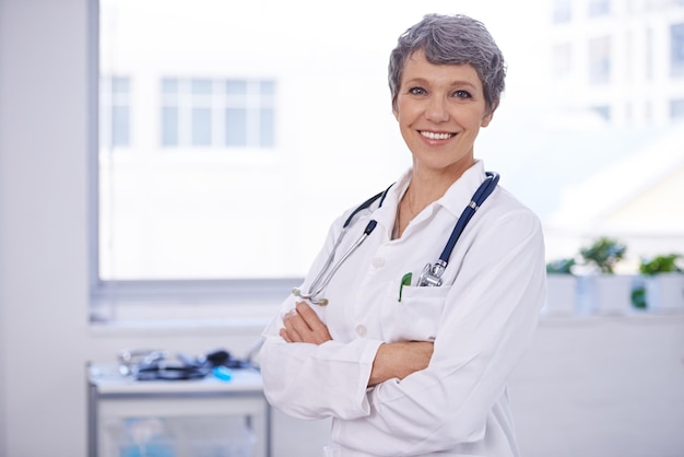 Ее медицинская практика хорошо организована. Снимок женщины-врача, стоящей в комнате со скрещенными руками.