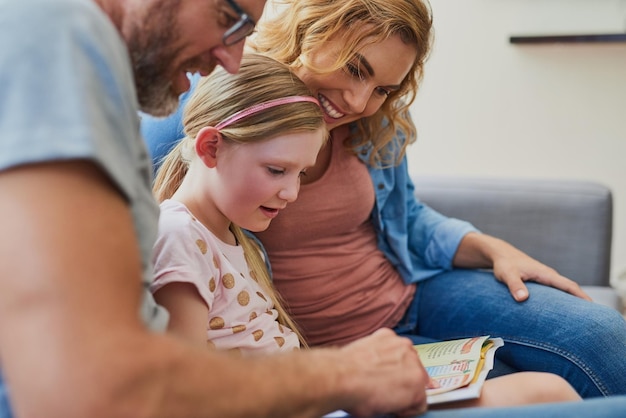 Her reading skills are improving thanks to her parents Cropped shot of a mother and father reading a book with their daughter on the sofa at home