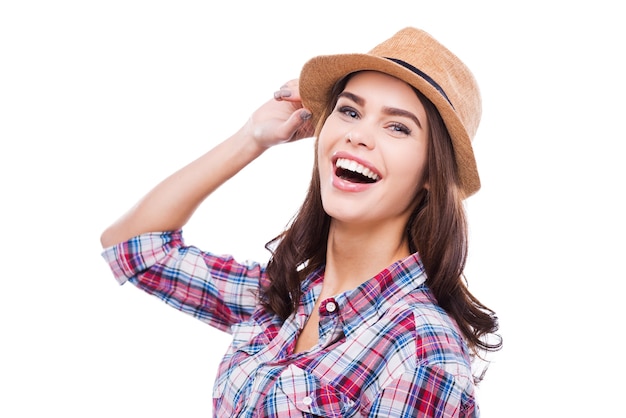 Il suo sorriso sta abbattendo. bella giovane donna in abbigliamento funky che regola il cappello e sorride alla macchina fotografica mentre sta in piedi su sfondo bianco