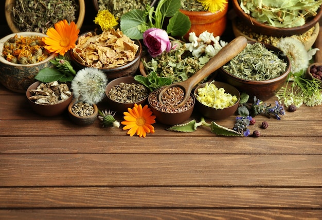 Herb selection and fresh flowers in bowls on wooden background