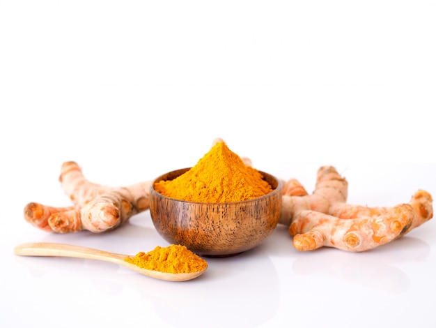 Erba con radice di curcuma e polvere di curcuma in ciotola e cucchiaio di legno isolato su superficie bianca con spazio di copia.