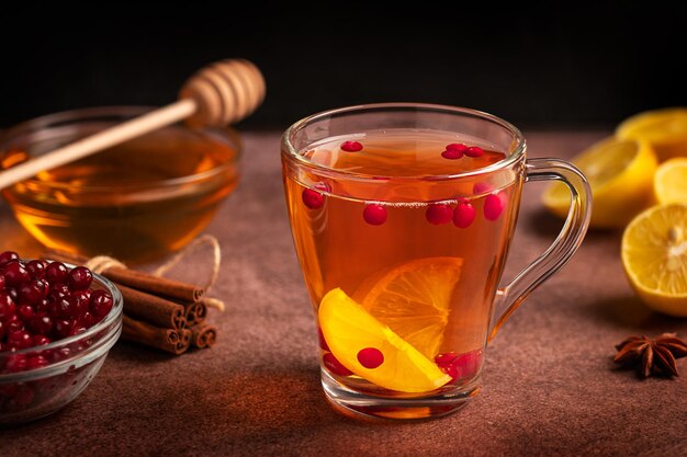 Herbal healthy vitamin hot tea with lemon slices, berries and honey served in cup on dark table