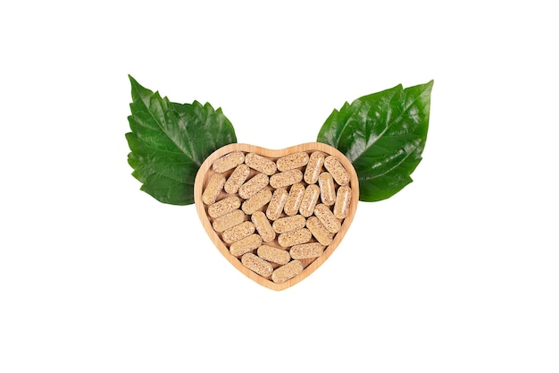 Photo herbal pills in heart shaped wooden plate and green leafs in the form of wings on blue background