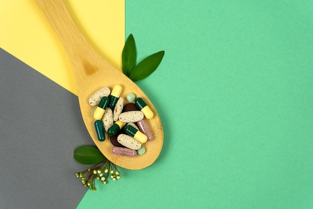 Herbal pills in a wooden spoon with herbs on colored backgrounds Alternative medicine vitamins