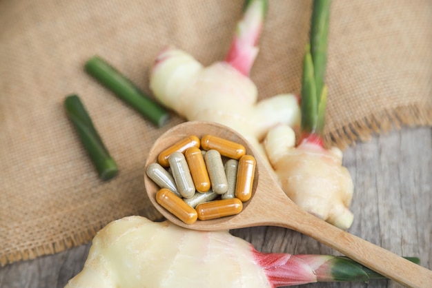 Herbal supplement in capsules with young ginger on wooden table for healthy medicine living