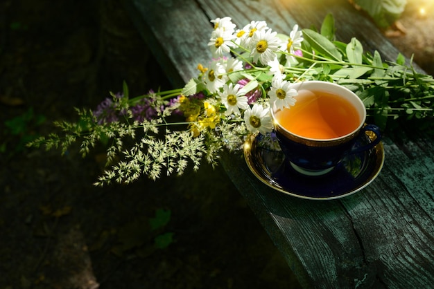夏の庭の木のテーブルにお茶と花束のカモミールの花と野の花を入れたハーブティーカップ