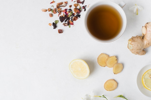Herbal tea cup with lemon; ginger; flower and dried petals ingredients on white background