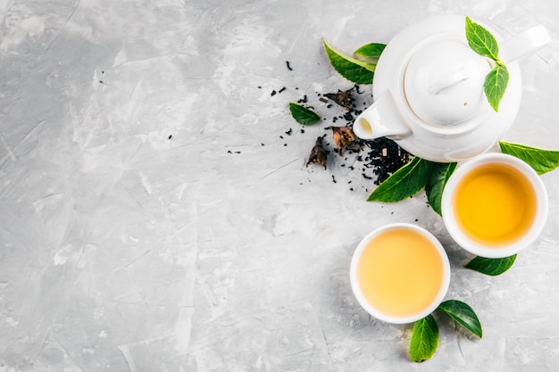 Photo herbal tea, cups and teapot with leaves on grey concrete background.