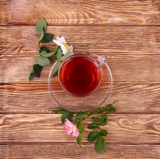 Herbal tea in a glass cup, fresh flowers on a background of wooden boards