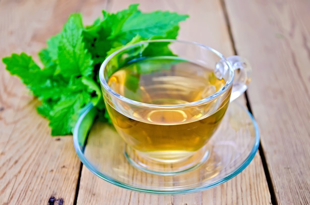 Herbal tea in glass cup, fresh melissa leaves on the background of wooden boards